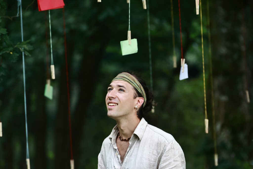 Un acteur Un homme souriant accroche des notes, illustrant l'harmonie entre nature et art au cœur d'un spectacle immersif De souvenirs en racine, montrant l'harmonie de l'engagement écologique