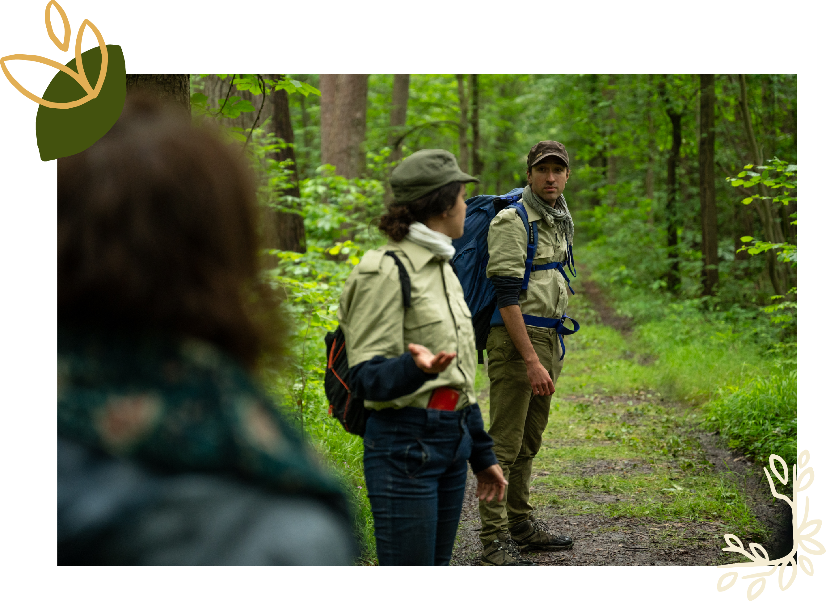 Deux gardes forestiers en pleine discussion dans une forêt verdoyante suivi du public. L'un d'eux se tourne vers ses compagnons, en désaccord sur la gestion forestière dans le cadre du spectacle déambulatoire de théâtre-paysage 'Les Écorcées si la forêt contait'