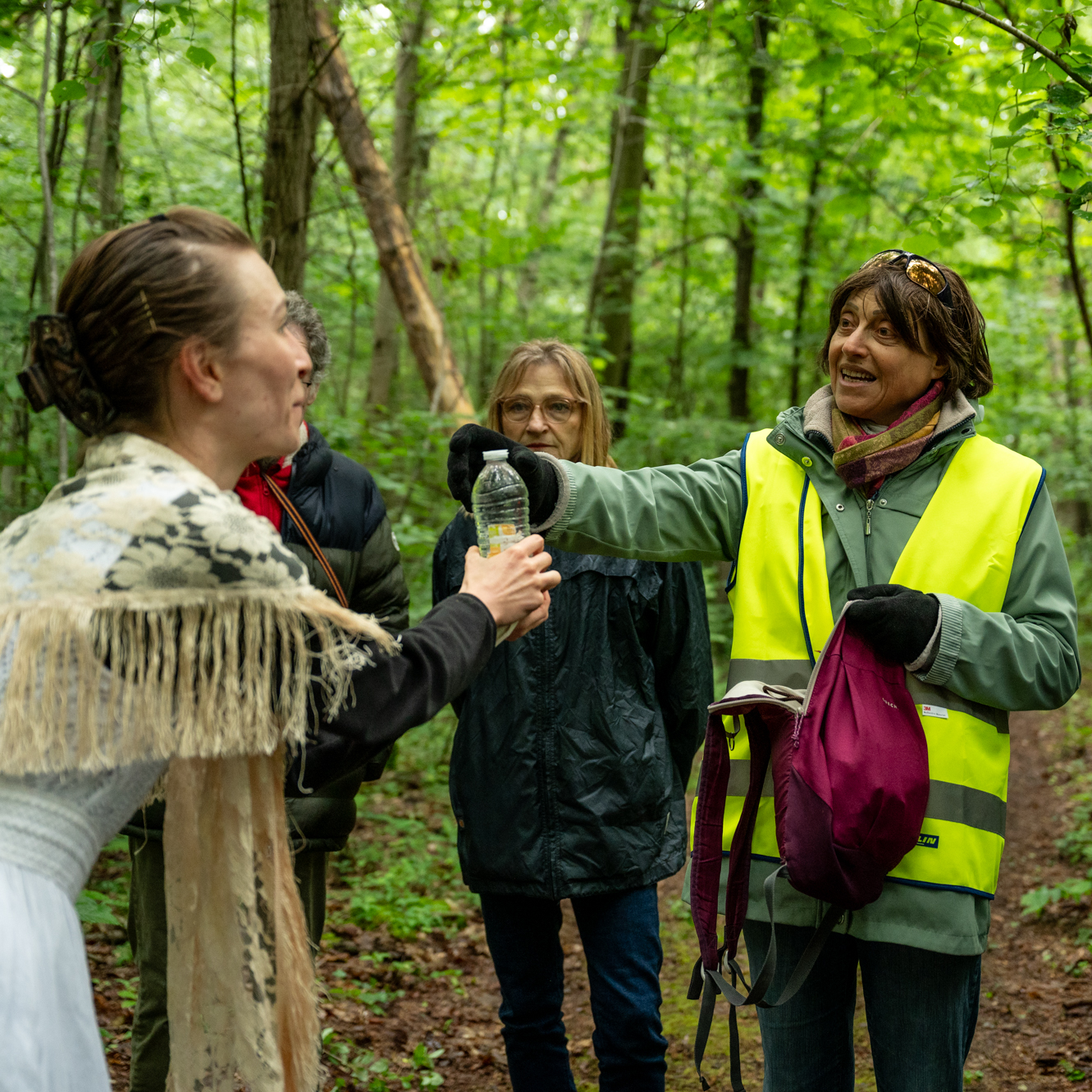 Une actrice vêtue de blanc interagit avec un membre du public lors d'une performance théâtrale en forêt. La rencontre se déroule dans le cadre immersif et éco-sensible de 'Les Écorcées', renforçant le lien entre nature et art.