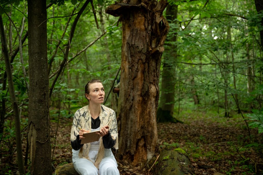Une actrice vêtue d'une robe blanche interagit avec le public lors du spectacle déambulatoire théâtre nature Les Écorcées en forêt