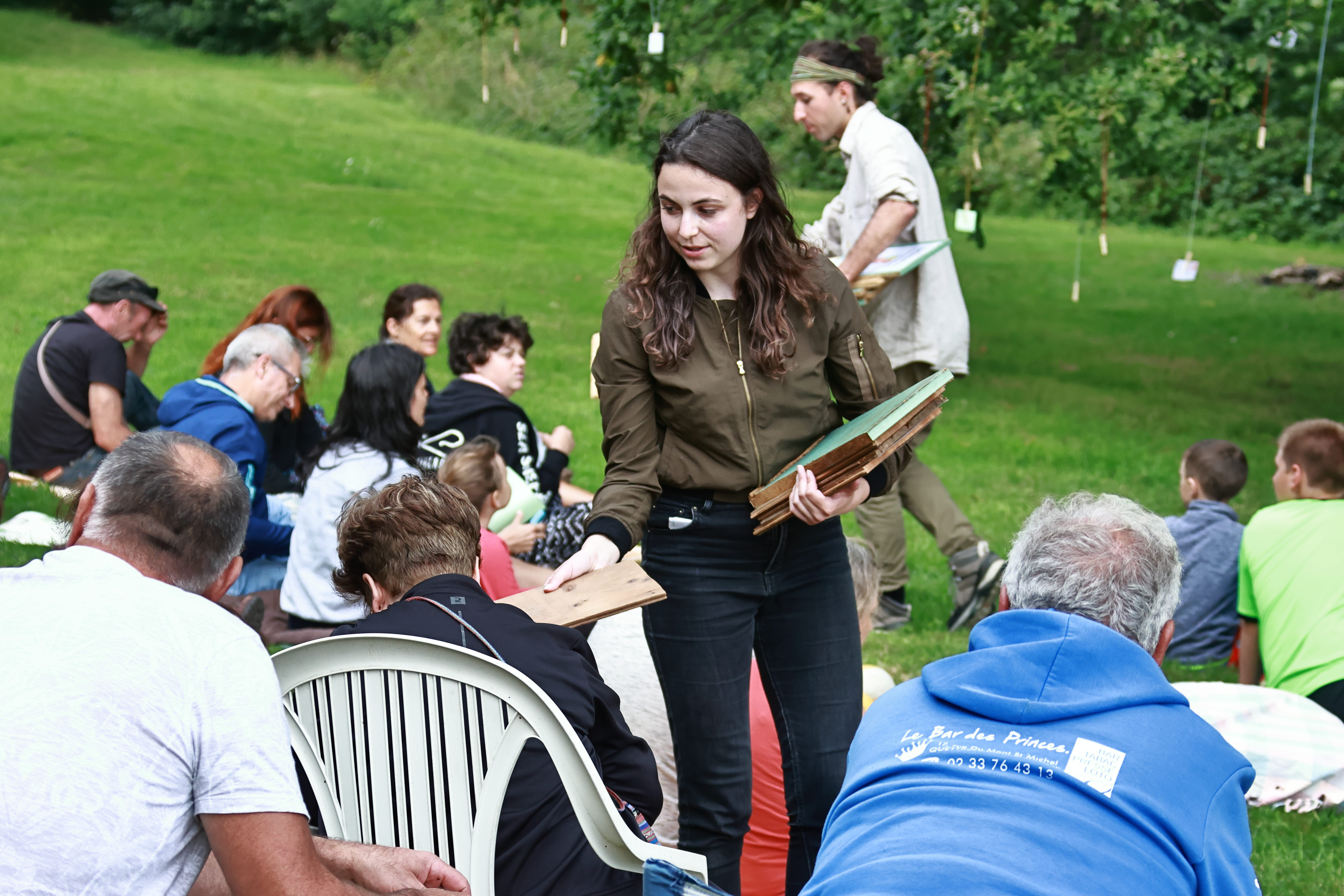 Une actrice distribue des papiers au public pour leurs souvenirssur les arbres et forêts du spectacle nature De Souvenirs en Racines