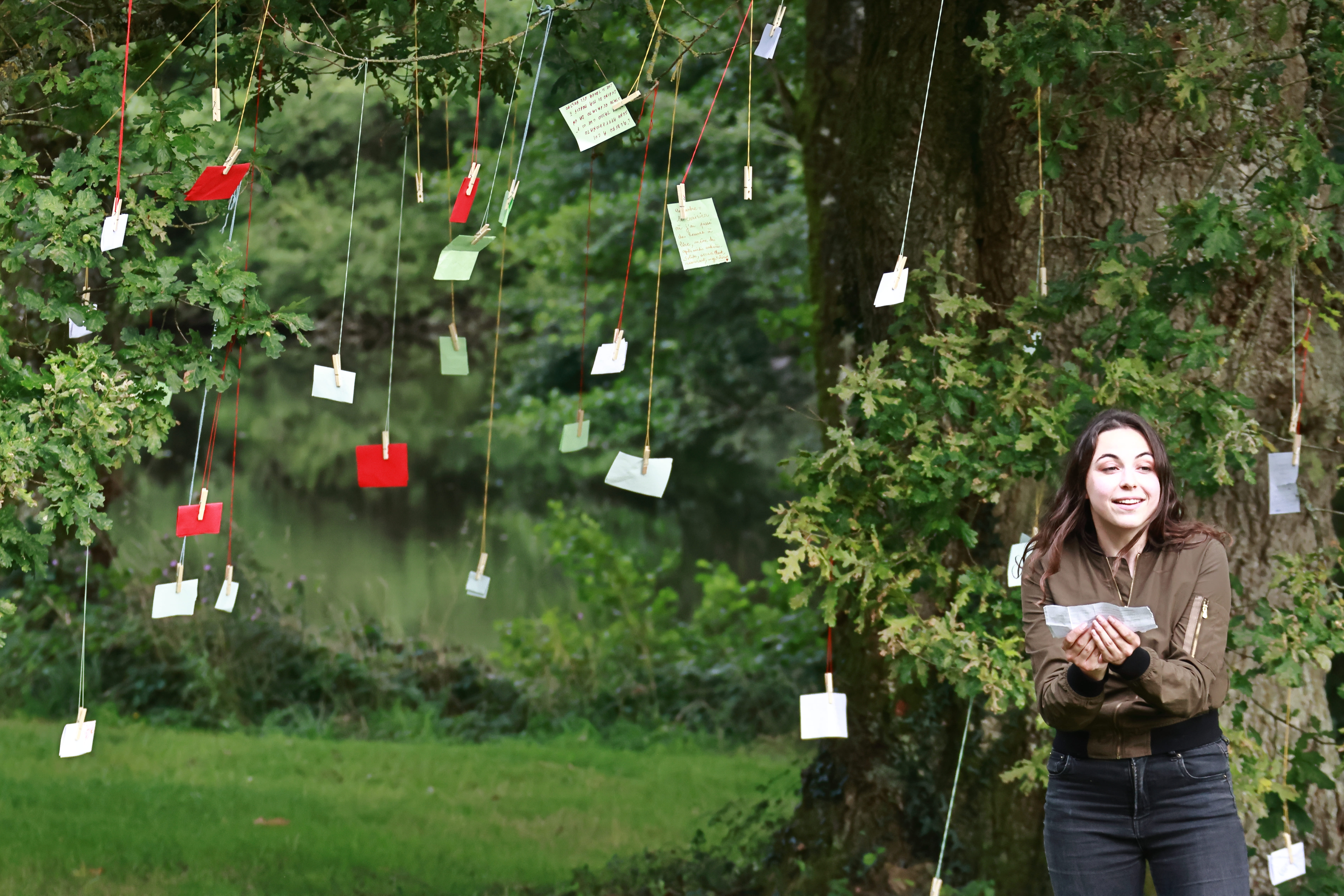 Une actrice lit un souvenir écologique accroché dans l'arbre dans une atmosphère poétique du spectacle nature De Souvenirs en Racines